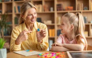 Happy woman speech therapist teaching little girl with pronounciation deffects to say sound R during personal training