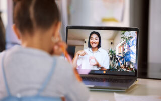 Little girl on a video call with her teacher using a laptop. Young female teacher doing a virtual lesson using blocks with her student. Little girl doing a virtual speech therapy session with a woman